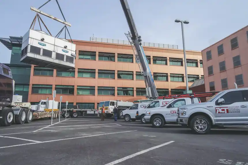 A crane lifting over a multi-storey brick building with ACT trucks in the lot