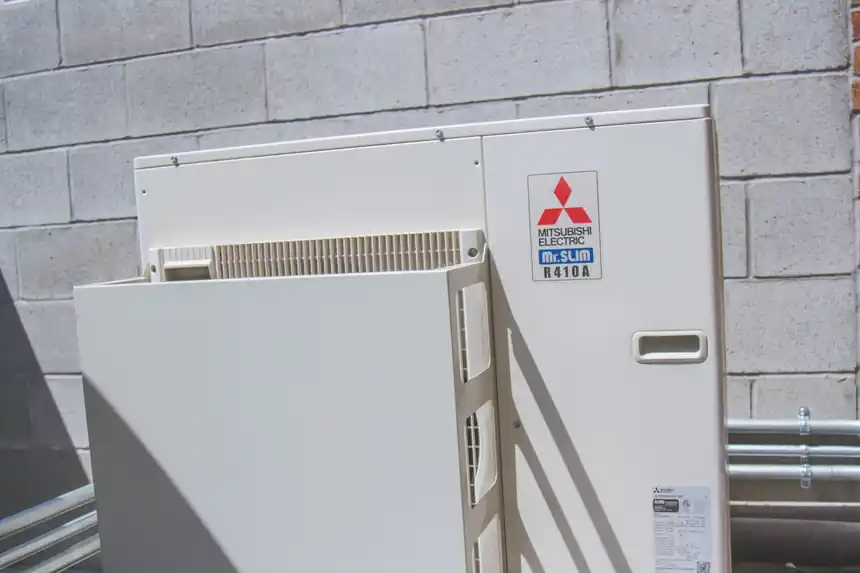 Mitsubishi outdoor condenser mounted beside a block wall