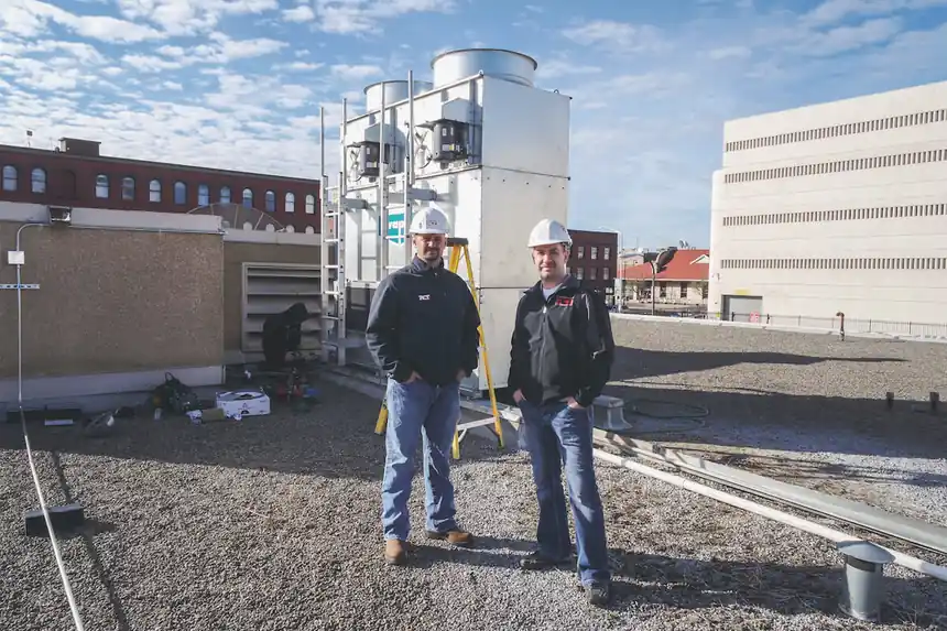 Two ACT techs in hard hats standing on the City Jail roof
