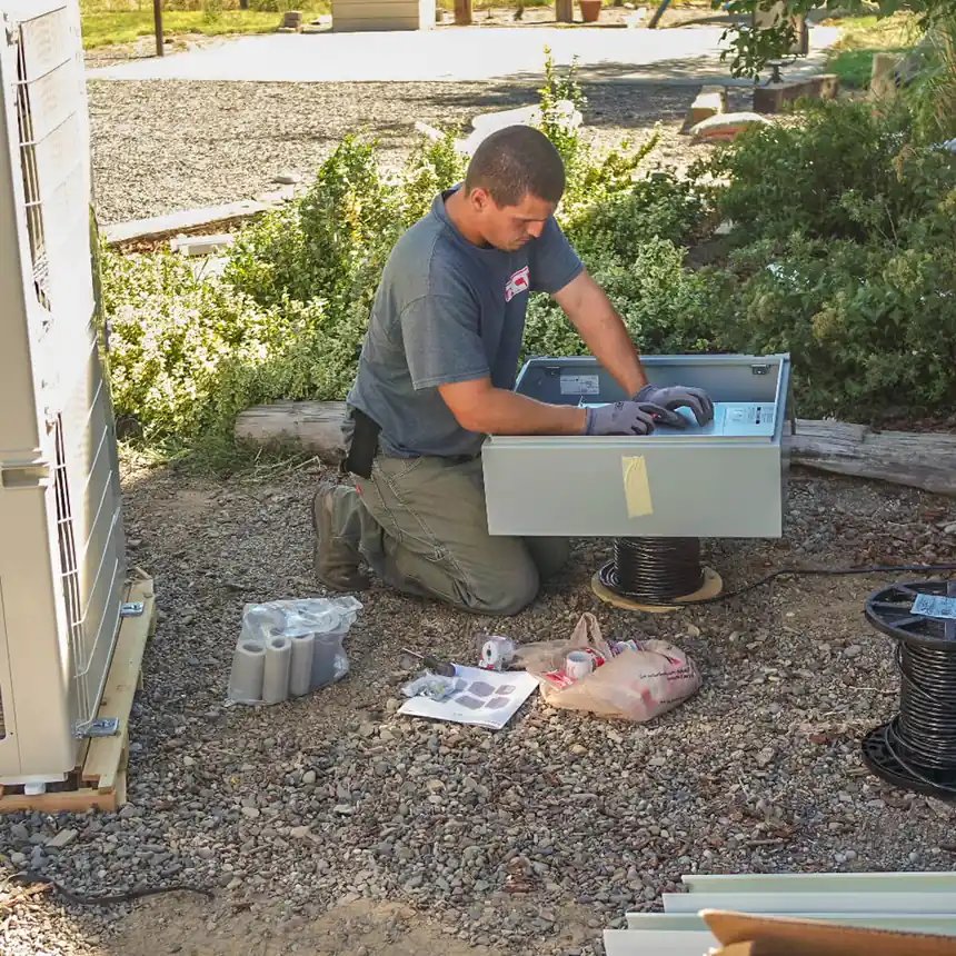 ACT technician kneeling to wire a Mitsubishi outdoor heat pump unit